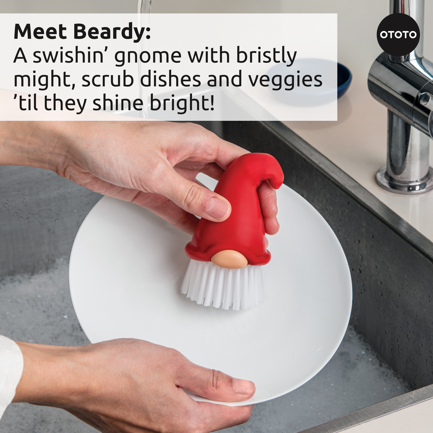 A hand cleans a white plate with the Forest Trio gnome-shaped dish brush in a kitchen sink.