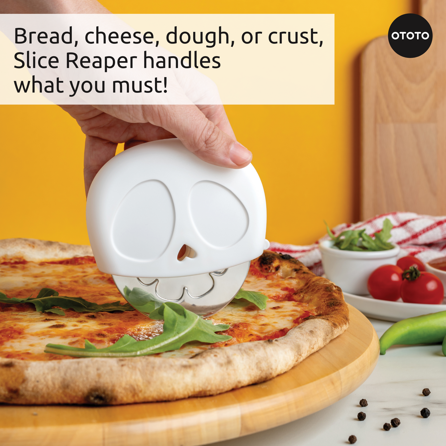 A hand slices pizza on a wooden board with the Slice Reaper pizza cutter, tomatoes nearby.