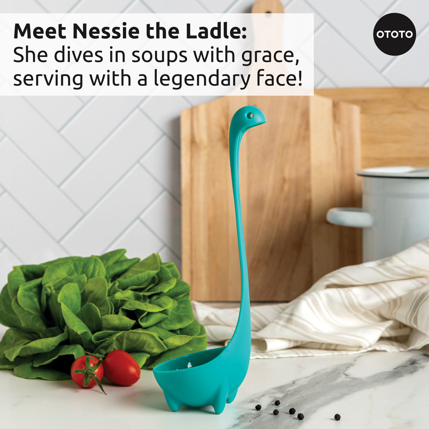 A blue Prep Pals ladle stands upright among veggies and kitchen tools on the counter.