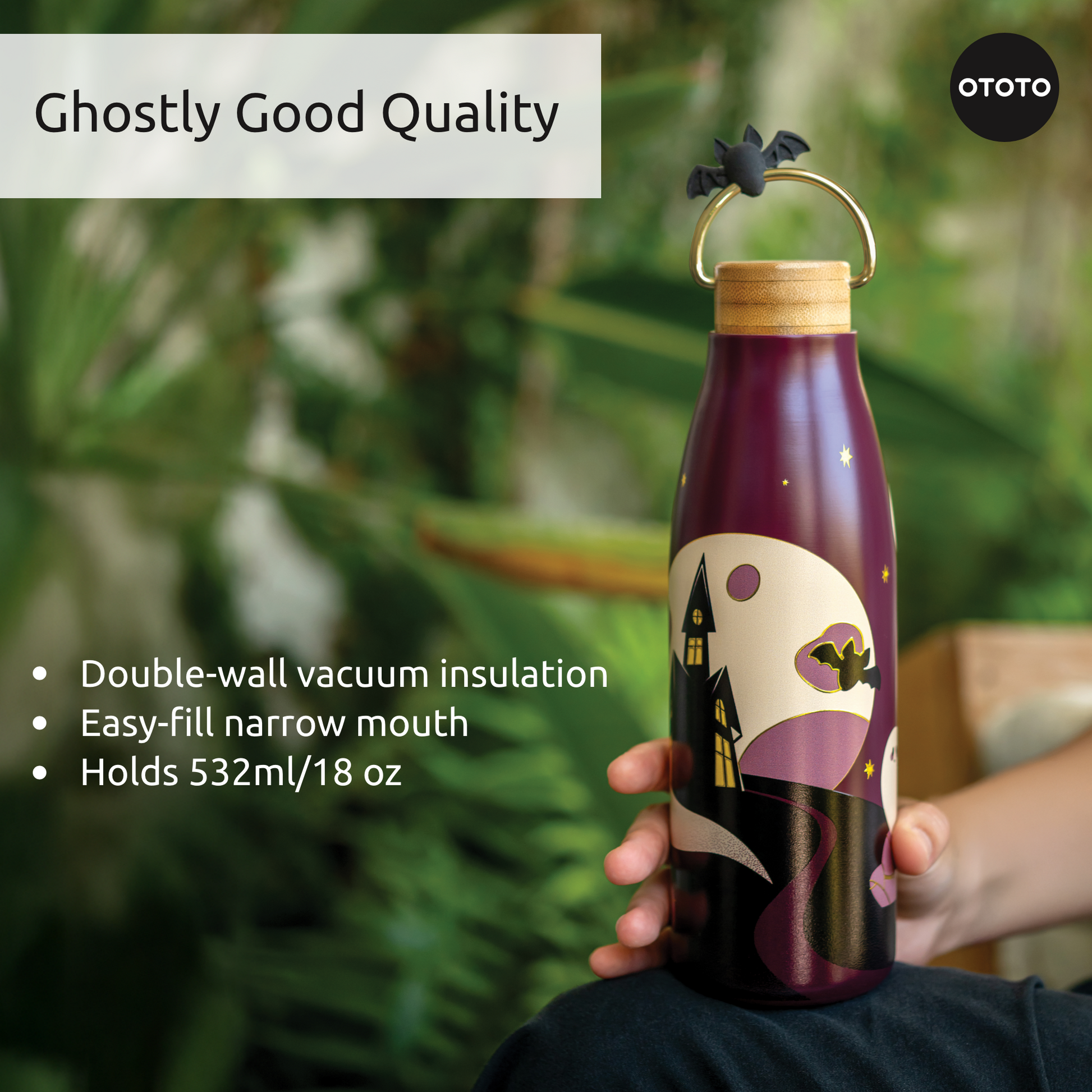 A hand holds the OTOTO Boo!tle insulated water bottle with a haunted house design and bat-shaped stopper.