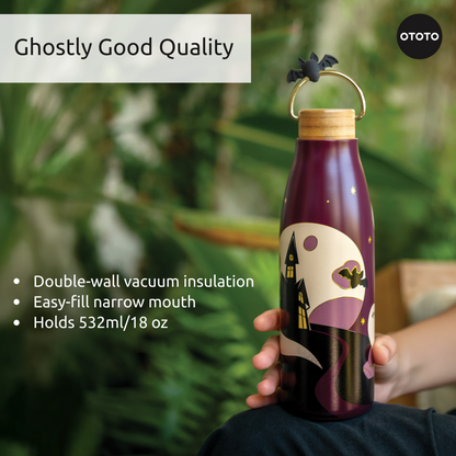 A hand holds the OTOTO Boo!tle insulated water bottle with a haunted house design and bat-shaped stopper.