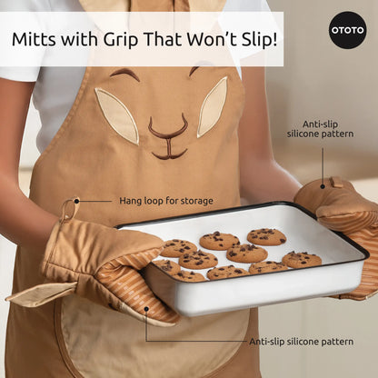 Person wearing Aproo bunny kitchen apron and oven mitts, holding a tray of chocolate chip cookies.