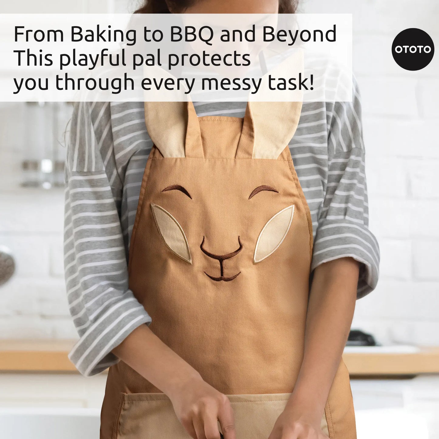 Person wearing an Aproo tan chef apron with floppy ears, in a kitchen with baking and BBQ text.