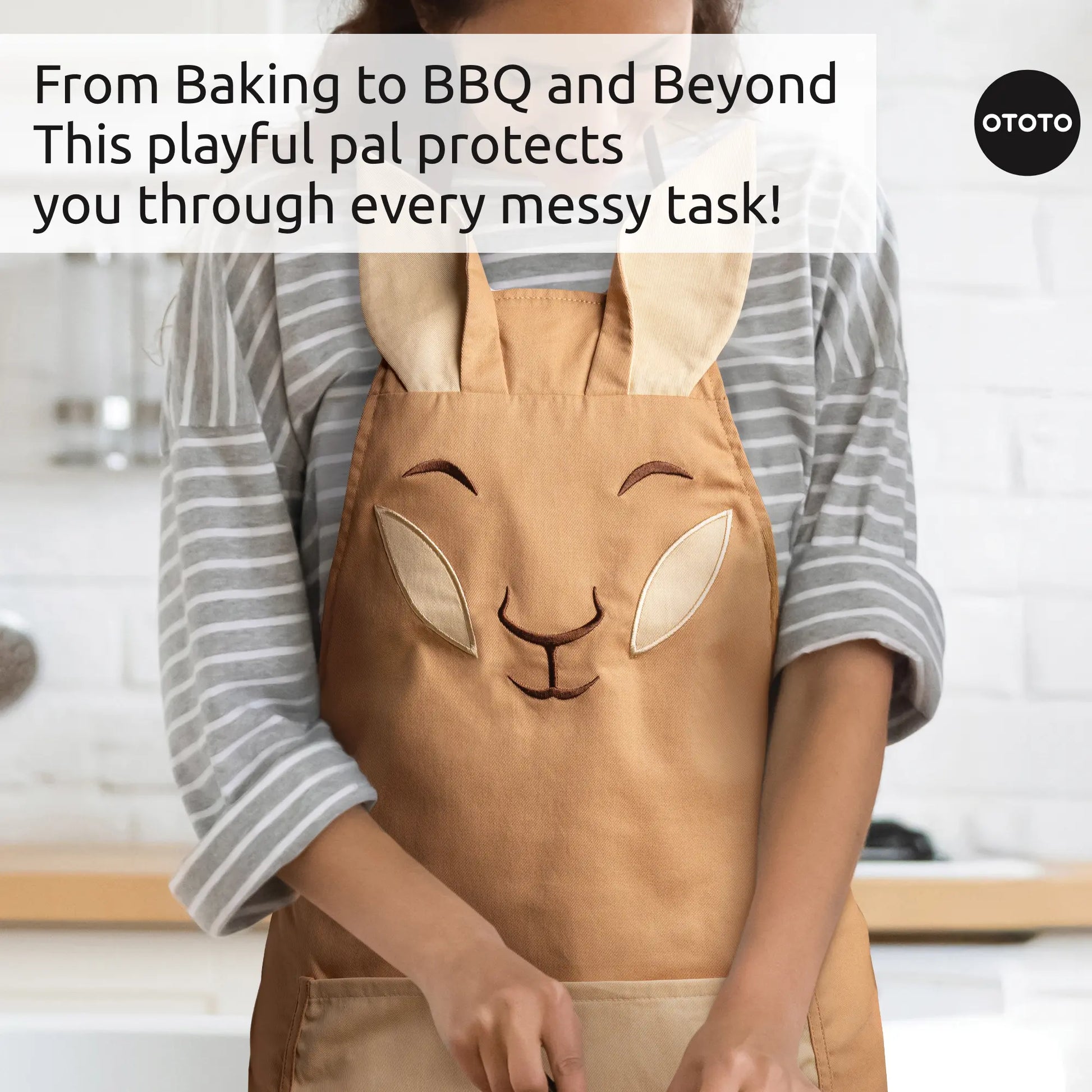 Person wearing an Aproo tan chef apron with floppy ears, in a kitchen with baking and BBQ text.
