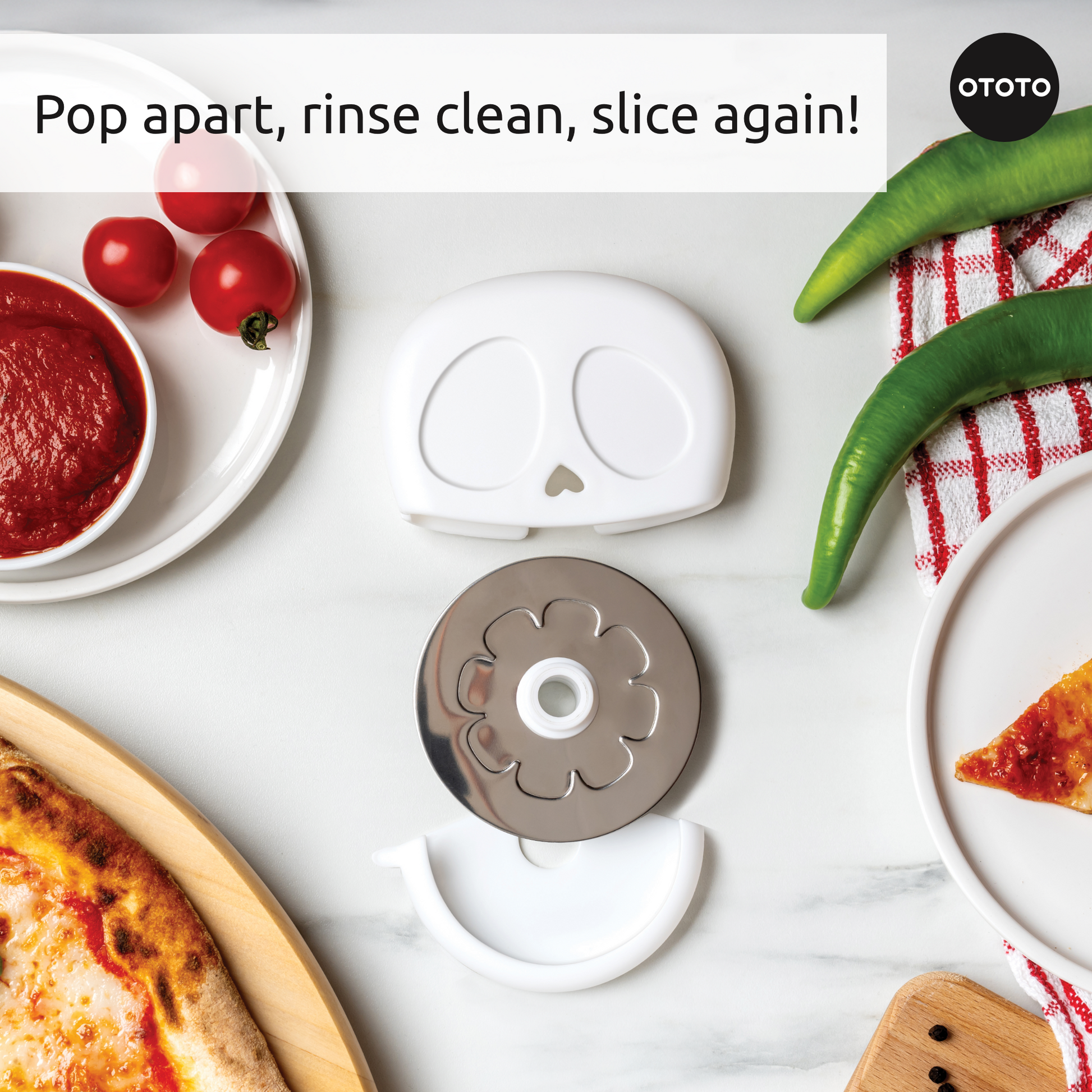 The Slice Reaper skull-shaped pizza cutter is disassembled next to pizza, sauce, tomatoes, and peppers.