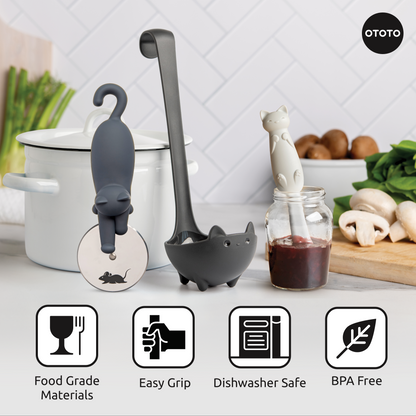 Three Muscateers cat-shaped utensils—a pizza cutter and ladle—sit on the counter near food.
