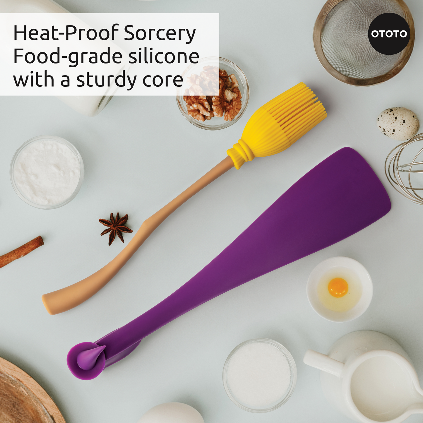 Two Witchin silicone spatulas sit on a countertop with baking ingredients and eggs.