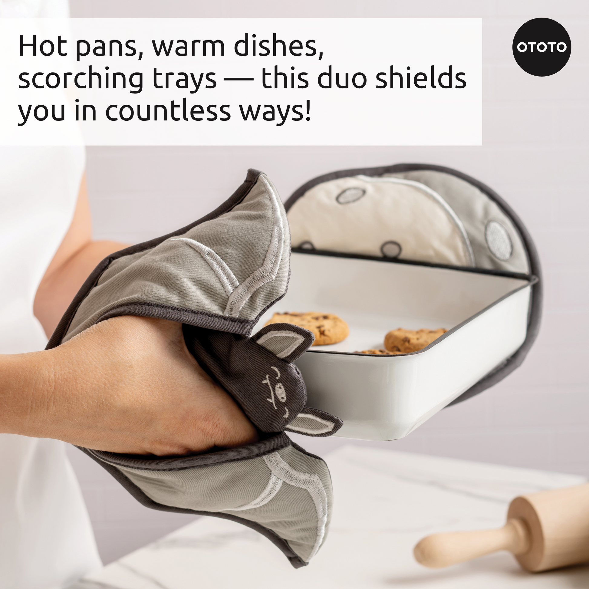 A person uses Batlicious oven mitts to hold a baking dish filled with cookies.