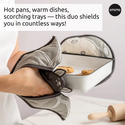 A person uses Batlicious cute animal-shaped oven mitts to hold a hot baking dish of cookies.