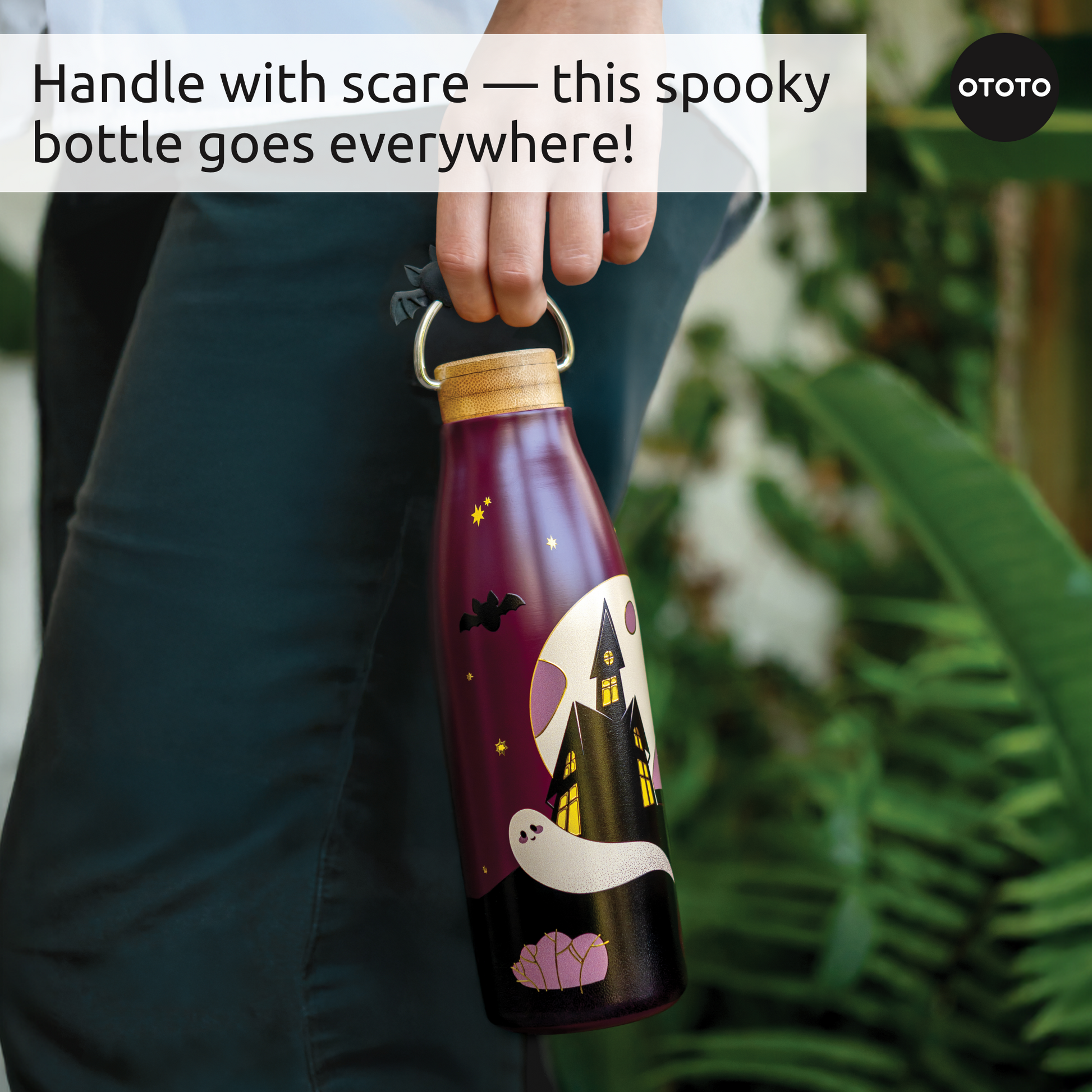 Someone holds a Boo!tle insulated water bottle with a spooky Halloween design amid greenery.