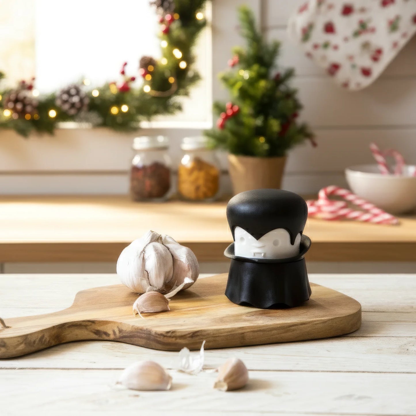 A garlic bulb and the Gracula garlic crusher rest on a wooden board in a festive kitchen.