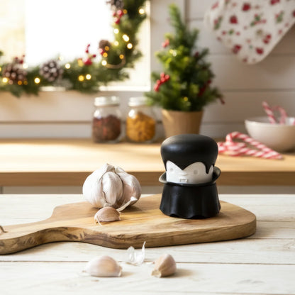 A garlic bulb and the Gracula garlic crusher rest on a wooden board in a festive kitchen.