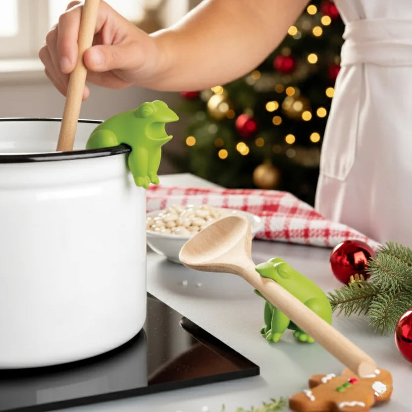 A person stirs a pot with a wooden spoon beside a HopTop froggy spoon rest on the stove.