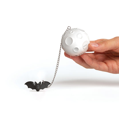 Hand holding the Moonlit Tea Infuser by OTOTO, with a chain and a small black bat attached.