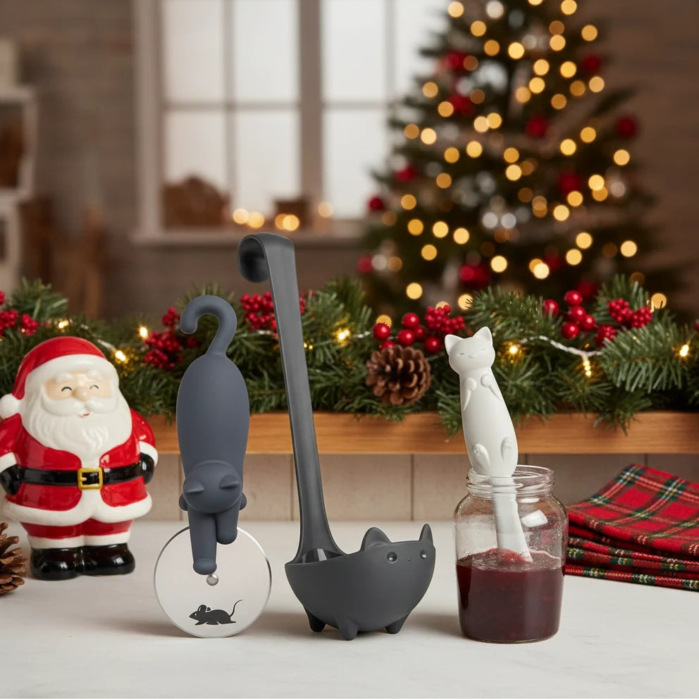 Muscateers cat-shaped soup ladle and pizza cutter on a counter with Santa and Christmas décor.