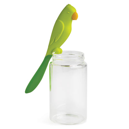 Parry, the green parrot-shaped silicone spatula by OTOTO, sits on a clear, empty glass jar.
