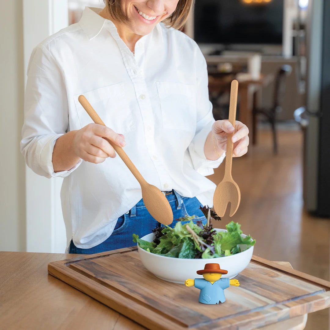 A woman tosses salad as Sal, an OTOTO scarecrow home accessory, stands by the bowl.