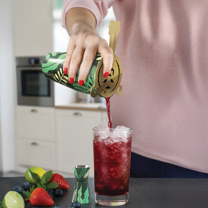 A home bartender pours a red drink over ice using the Sip Safari cocktail shaker set, fruit nearby.
