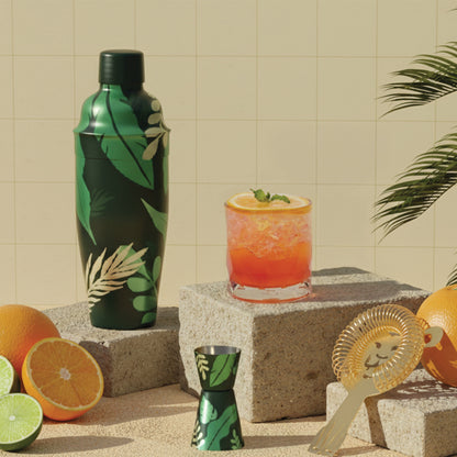 Sip Safari green cocktail shaker set and bar accessories are styled with drinks on concrete blocks.
