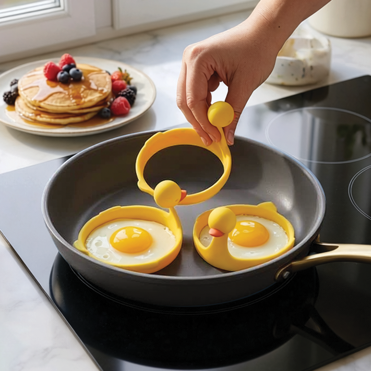 A hand uses the Sunny Side Duck to cook sunny-side-up eggs in a frying pan.