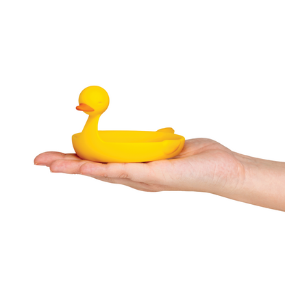 A hand holds the Sunny Side Duck, a small yellow duck-shaped egg separator, against a white background.