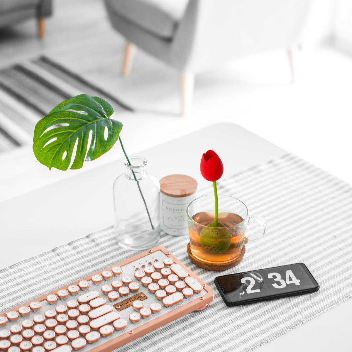 Vintage keyboard, smartphone, and Tulip tea infuser in cup on striped table runner with vase.