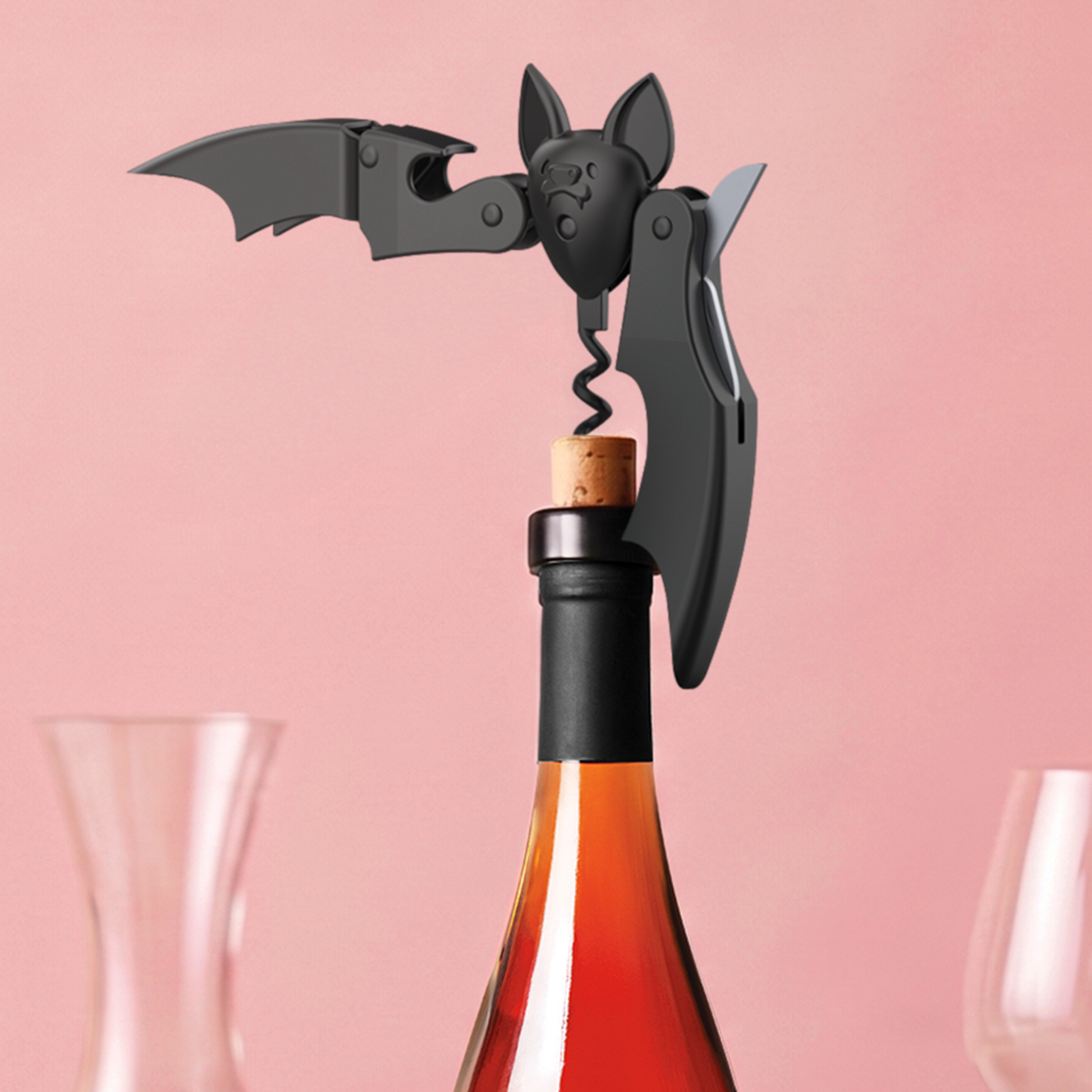 Vino bat-shaped OTOTO corkscrew opens a wine bottle, glassware softly blurred in the background.