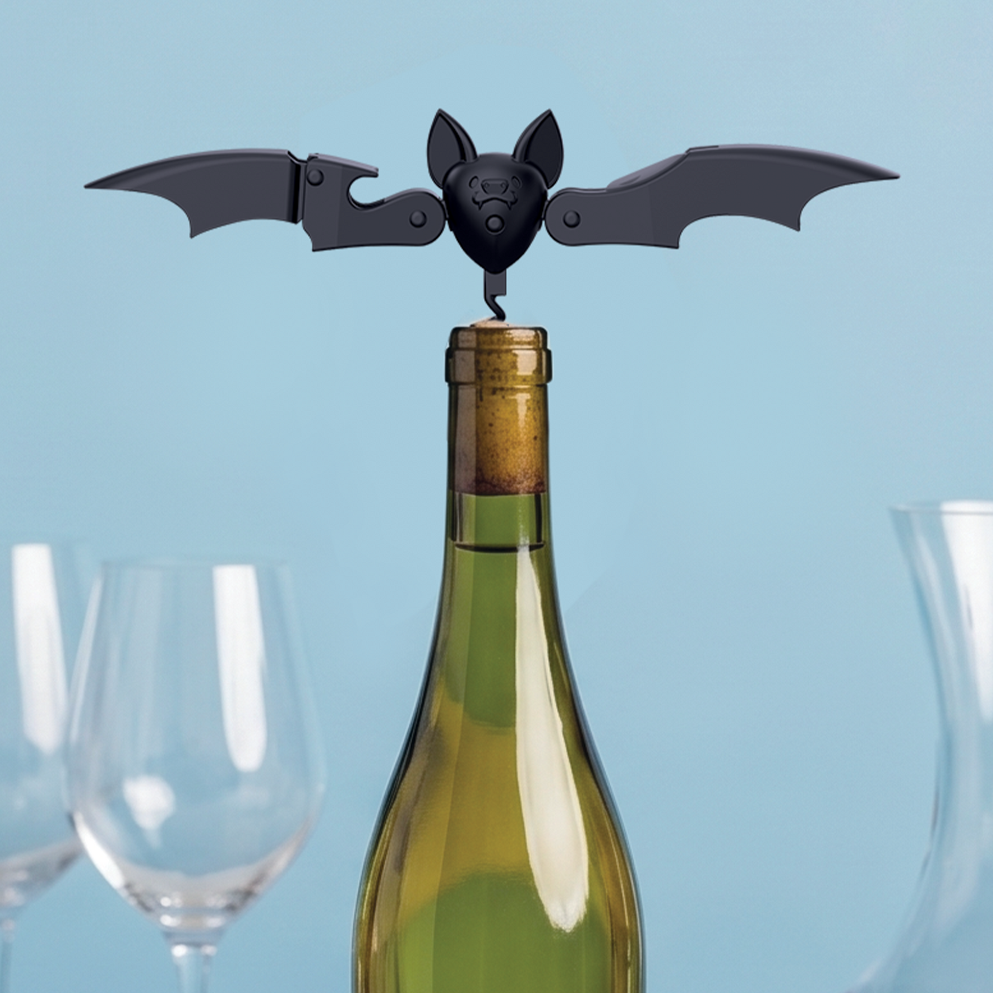 Vino, the OTOTO bat-shaped corkscrew, perches on a wine bottle with empty glasses awaiting a pour.