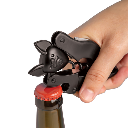 Hand using an OTOTO Vino black bat-shaped bottle opener to open a capped glass bottle.