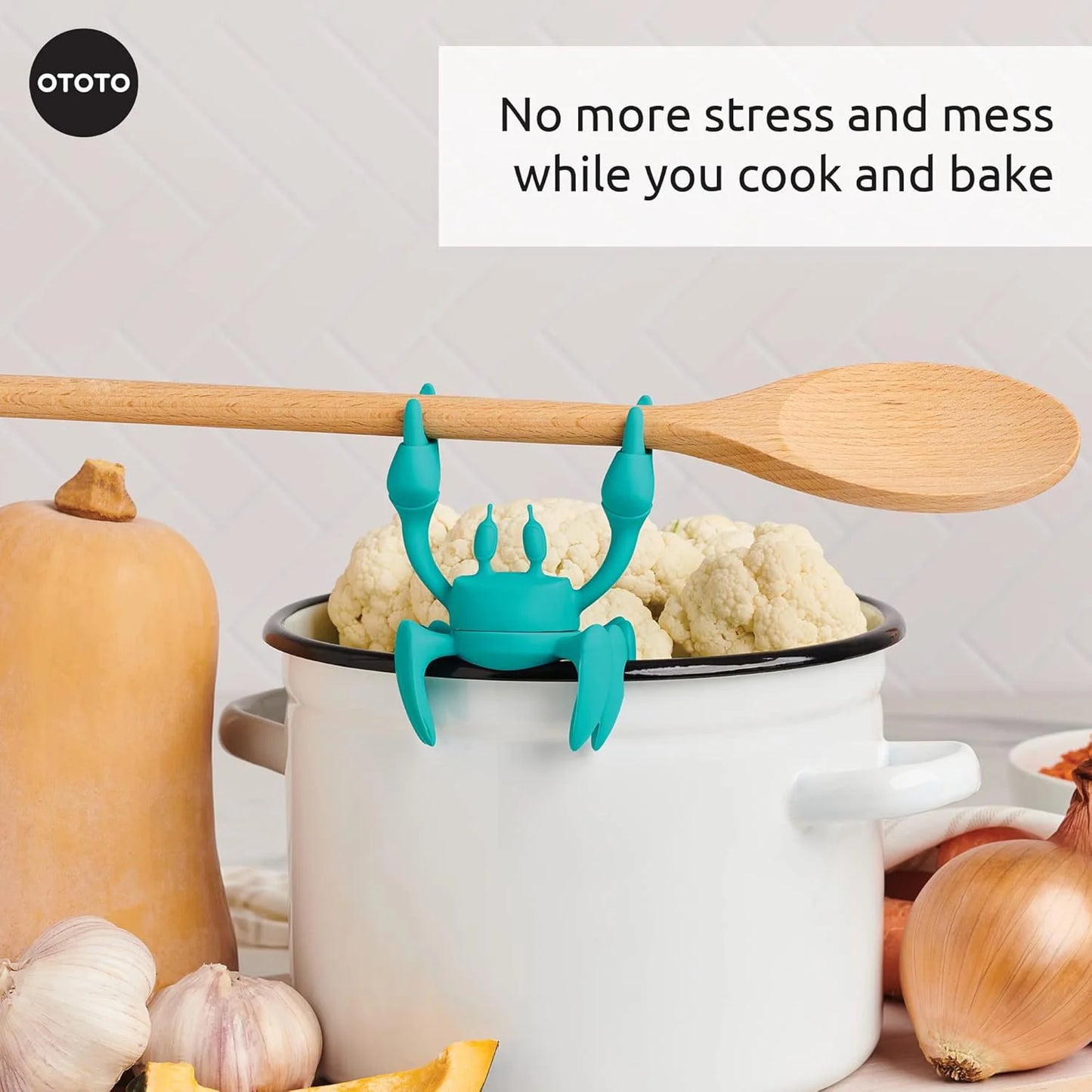 Aqua, a blue crab-shaped silicone utensil rest by OTOTO, grips a wooden spoon; veggies nearby.