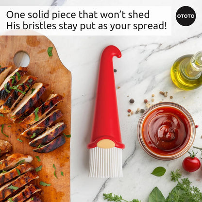 A red OTOTO Gnomeo pastry brush with sliced grilled chicken on a wooden board, herbs, oil, and sauce.
