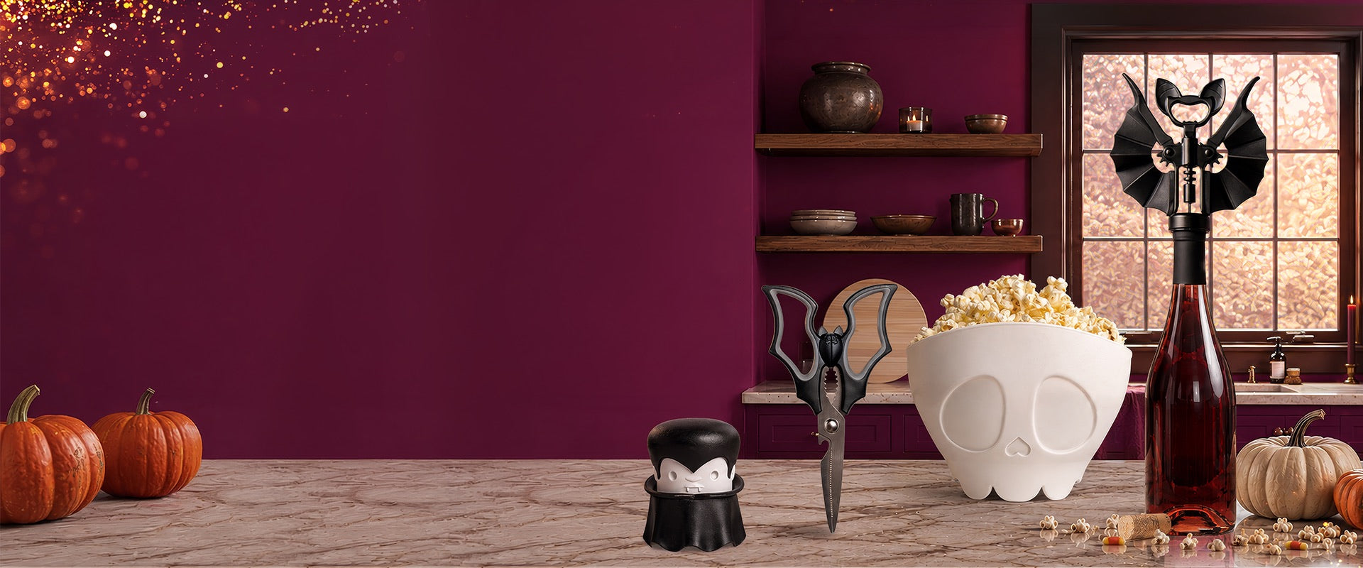 OTOTO's spooky kitchen on a marble counter with pumpkins: a Dracula garlic crusher, bat kitchen scissors, a skull popcorn bowl and a bat corkscrew on a bottle of red wine